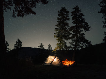 Sky View stargazing tent at dusk with dark sky full of stars and a campfire with trees 