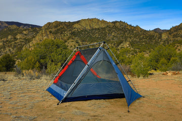 The Sky View XL stargazing camping tent sits on level ground in front of mid-sized mountains in the background on a sunny day.