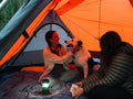 Two people inside an orange tent with a dog.