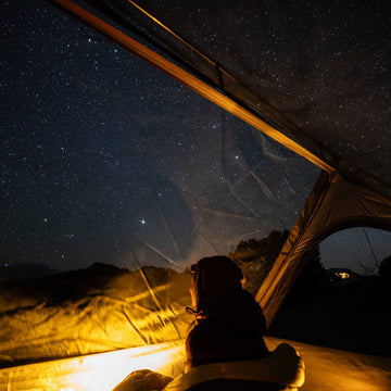 Person sitting inside a tent looking up at a starry night sky